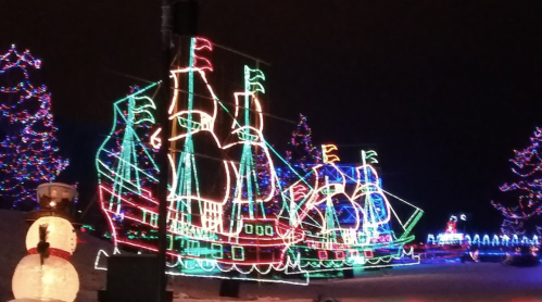 Colorful holiday lights depict a large ship surrounded by decorated trees and a snowman in a festive winter scene.