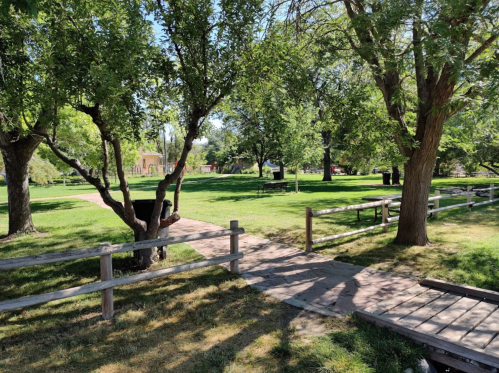 A sunny park scene with green trees, a grassy area, and a wooden fence along a path leading to benches.