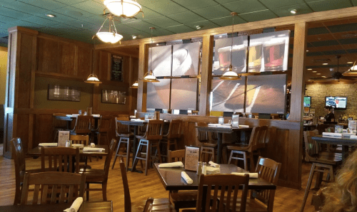 Interior of a restaurant featuring wooden tables, chairs, and wall decor with images of food and drinks.