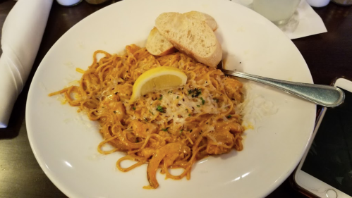 A plate of creamy pasta with shrimp, garnished with lemon and parsley, served with two slices of bread.