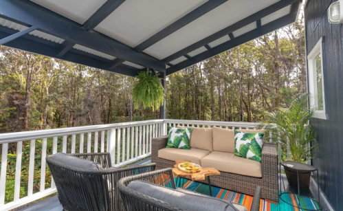 Cozy outdoor seating area with a sofa and chairs, surrounded by greenery and a colorful rug.
