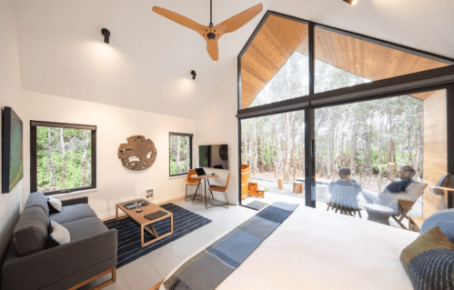 Modern cabin interior with large windows, a cozy seating area, and a view of a forested outdoor space.