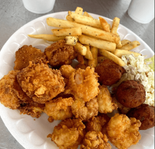 A plate of fried seafood, including shrimp and fish, with fries, coleslaw, and hushpuppies.