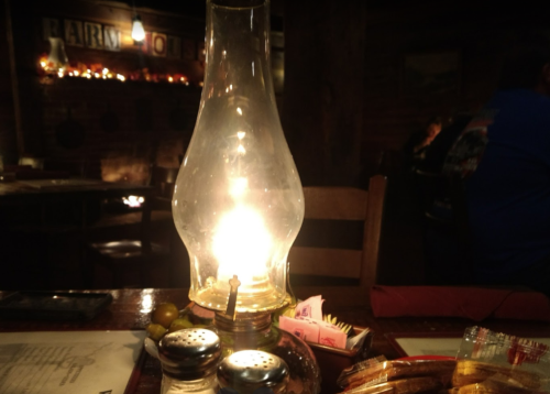 A glowing oil lamp on a wooden table, surrounded by condiments and snacks in a cozy, dimly lit restaurant.