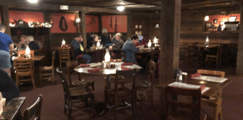 Cozy restaurant interior with wooden decor, tables set for dining, and patrons enjoying their meals. Warm, inviting atmosphere.