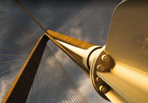 A close-up view of a modern suspension bridge's tower and cables against a cloudy sky.