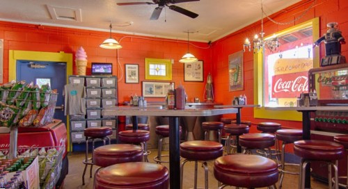 A colorful diner interior with red walls, bar stools, a Coca-Cola sign, and a vintage ice cream machine.