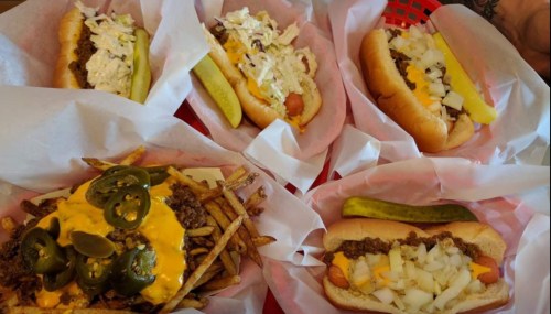 A spread of hot dogs topped with various ingredients, served with a side of cheesy fries and jalapeños.