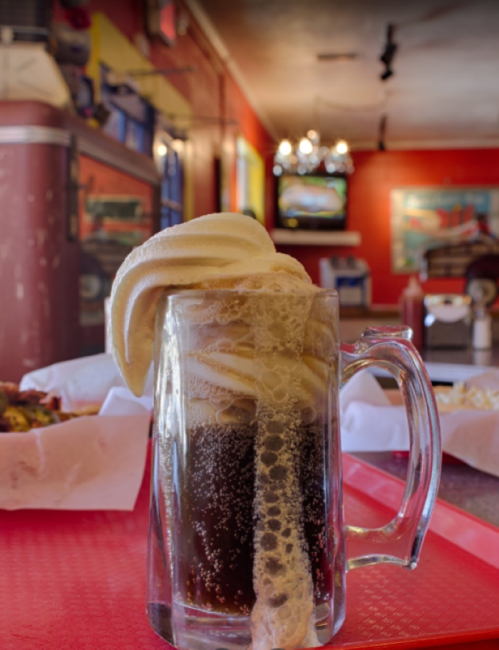A frosty mug of root beer topped with creamy vanilla ice cream, set on a red tray in a colorful diner.