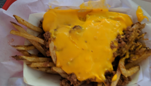 A serving of French fries topped with melted cheese and ground beef in a white tray.