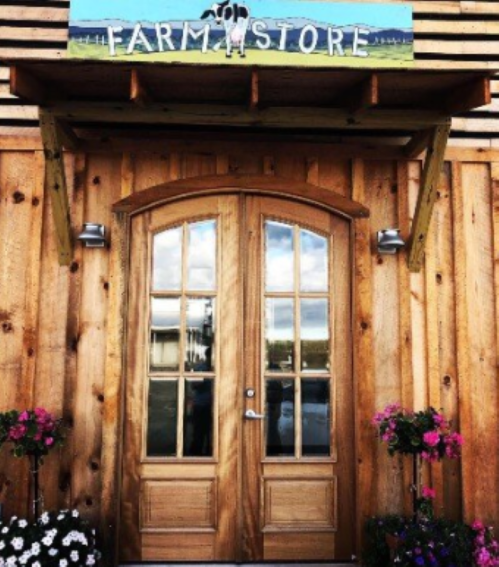 A wooden door with large windows, leading to a farm store, surrounded by colorful flowers and a blue sky.