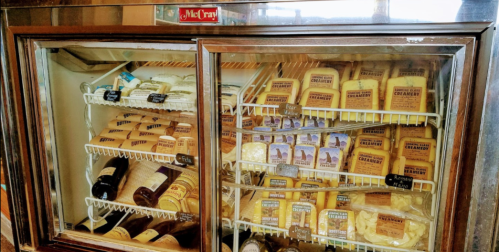 A glass-front refrigerator filled with various cheeses and bottles, showcasing a variety of dairy products.