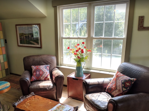 Cozy living room with two armchairs, a wooden table, and a vase of flowers by the window, letting in natural light.