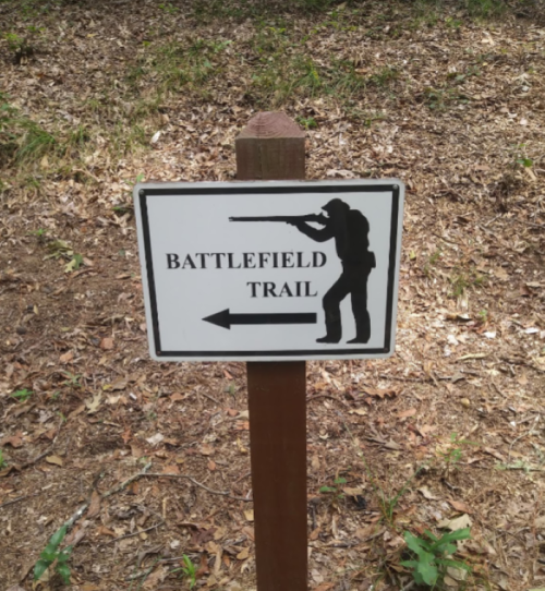 Sign for "Battlefield Trail" with an arrow pointing left, featuring a silhouette of a soldier aiming a rifle.