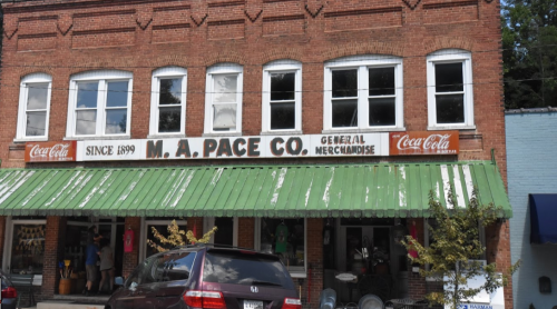 Historic brick building with a green awning, featuring "M.A. Pace Co. General Merchandise" and Coca-Cola signage.