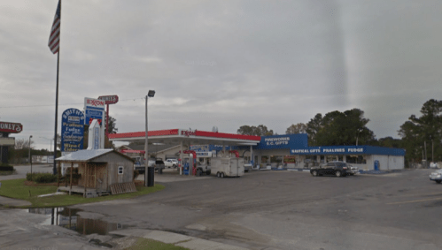 Gas station with convenience store, flagpole, and nearby gift shop, set in a rural area with cloudy skies.
