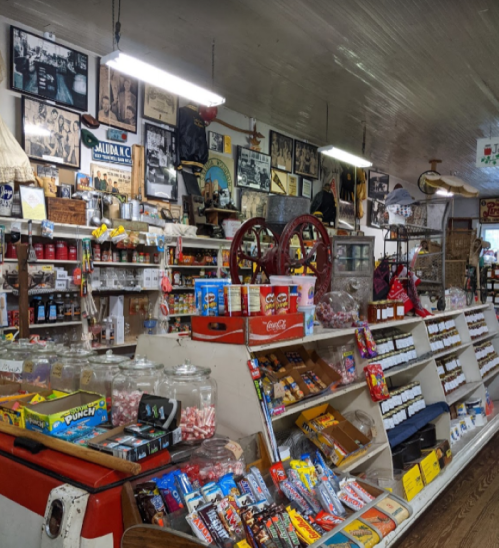 A vintage general store filled with candy, snacks, and nostalgic decor, featuring shelves and old photographs on the walls.