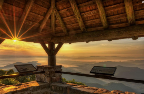 Sunrise view from a wooden lookout, with mountains and mist in the distance, illuminated by golden sunlight.