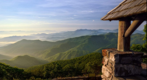A scenic view of rolling green mountains under a clear sky, with a wooden structure in the foreground.