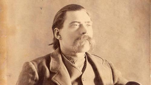 A sepia-toned portrait of a man with a mustache, wearing a suit and looking thoughtfully to the side.