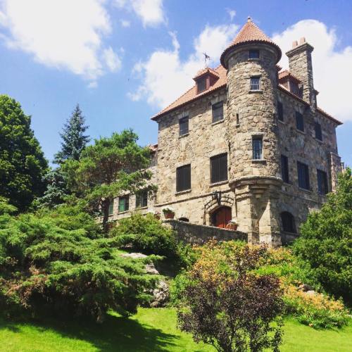 A stone mansion with a turret, surrounded by lush greenery and colorful flowers under a bright blue sky.