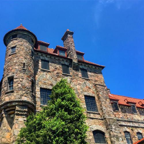 Historic stone building with a turret, red tile roof, and clear blue sky in the background.