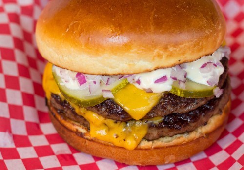 A close-up of a juicy cheeseburger with two patties, melted cheese, pickles, and onions on a toasted bun.