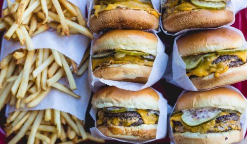 A close-up of three cheeseburgers with pickles and onions, alongside a serving of golden French fries.