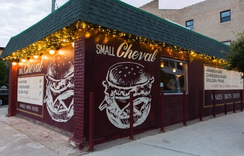 Exterior of Small Cheval restaurant, featuring a burger mural and string lights, with a menu displayed on the wall.