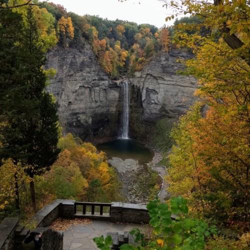 A scenic view of a waterfall surrounded by colorful autumn foliage and rocky cliffs.