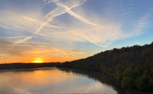 Sunset over a calm lake, with colorful clouds and trees lining the shore, reflecting on the water's surface.