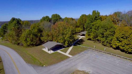 Aerial view of a park with two buildings surrounded by trees and a paved road. Clear blue sky above.