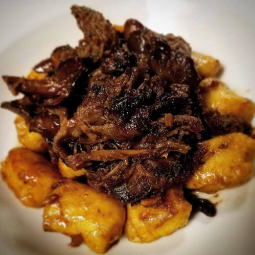 A plate of tender shredded meat served over golden, fried dumplings, garnished with dark sauce and mushrooms.