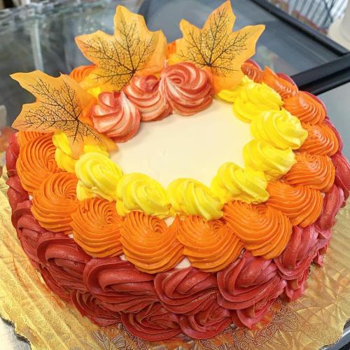 A round cake decorated with vibrant red, orange, and yellow frosting, topped with edible autumn leaves.