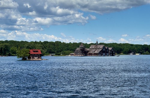 A scenic view of a lake with a small red-roofed building on an island and a large, historic structure in the background.