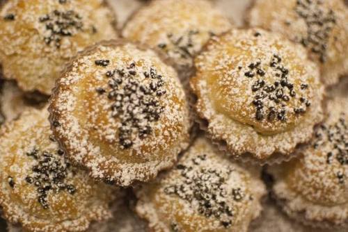 A close-up of freshly baked muffins topped with powdered sugar and black seeds, arranged in a pile.