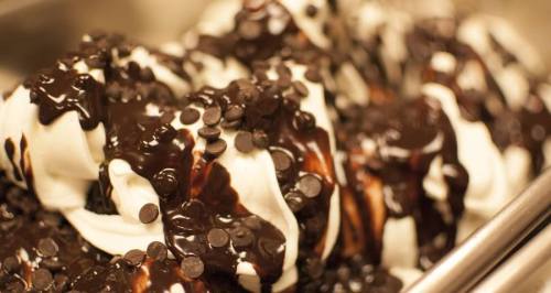 A close-up of soft-serve ice cream drizzled with chocolate sauce and topped with chocolate chips.