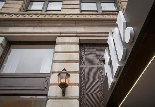 Signage on a historic building featuring modern lettering and a decorative wall panel, with a lantern light fixture.