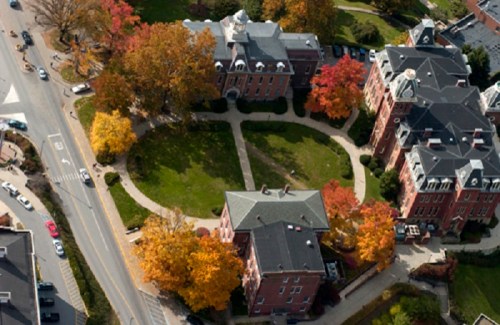 Aerial view of a campus with red brick buildings and colorful autumn trees surrounding a central green space.