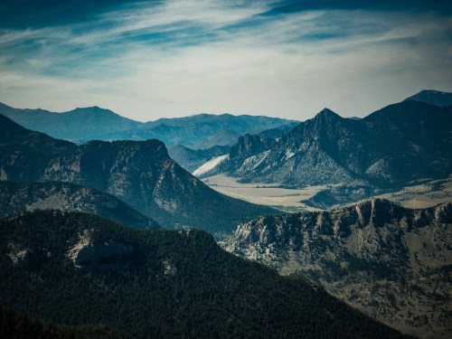 A panoramic view of rugged mountains and valleys under a cloudy sky, showcasing natural beauty and diverse terrain.