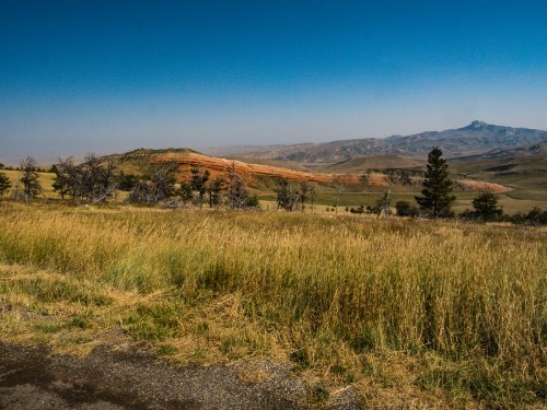 A vast landscape featuring rolling hills, grassy fields, and distant mountains under a clear blue sky.