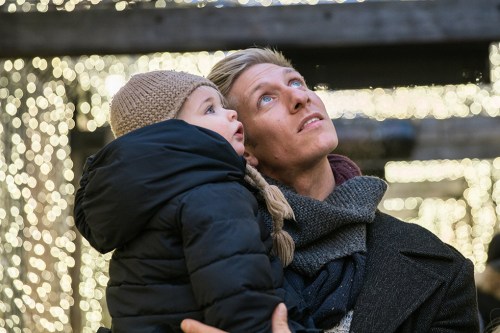 A man and a child gaze up in wonder at twinkling lights in a festive setting.