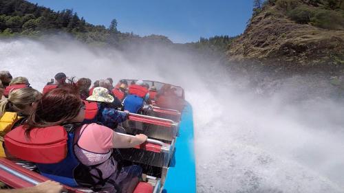 A group of people in life jackets on a speedboat, splashing through water with a scenic backdrop of trees and cliffs.