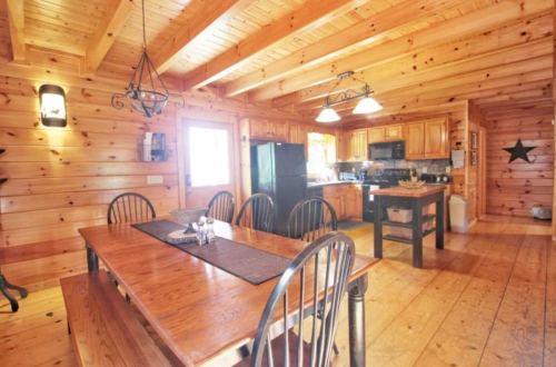 Cozy wooden kitchen with a dining table, black appliances, and warm lighting in a rustic cabin setting.
