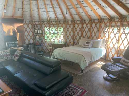 Cozy yurt interior featuring a bed, seating area, and rustic decor with natural light streaming through the windows.