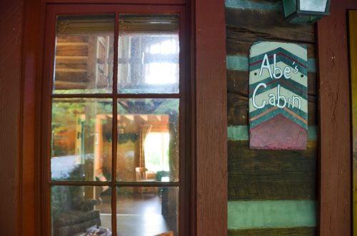 A rustic cabin interior with a sign reading "Abe's Cabin" next to a window reflecting the cozy space inside.
