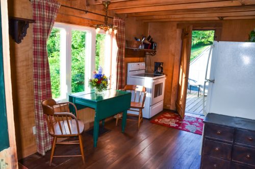 Cozy kitchen with a green table, two chairs, a white fridge, and large windows overlooking greenery.