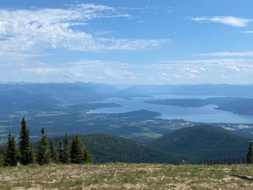 A panoramic view of a lake surrounded by mountains and lush greenery under a blue sky with scattered clouds.
