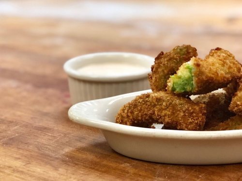 A plate of golden-brown fried snacks with a green filling, served with a small bowl of dipping sauce.