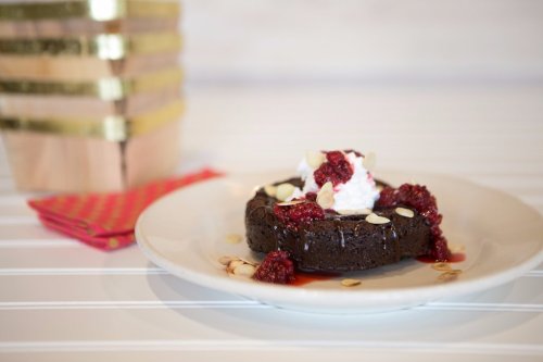 A chocolate dessert topped with raspberry sauce, whipped cream, and sliced almonds on a white plate.